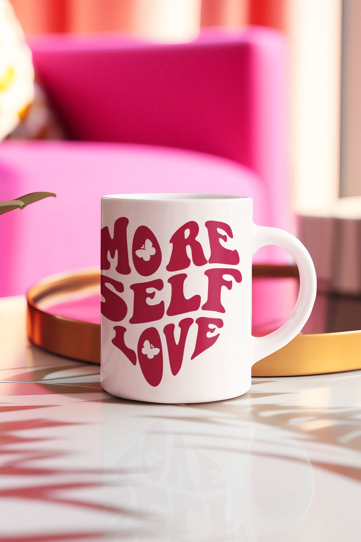 More Self Love butterfly coffee mug styled on a table with pink chair in the background