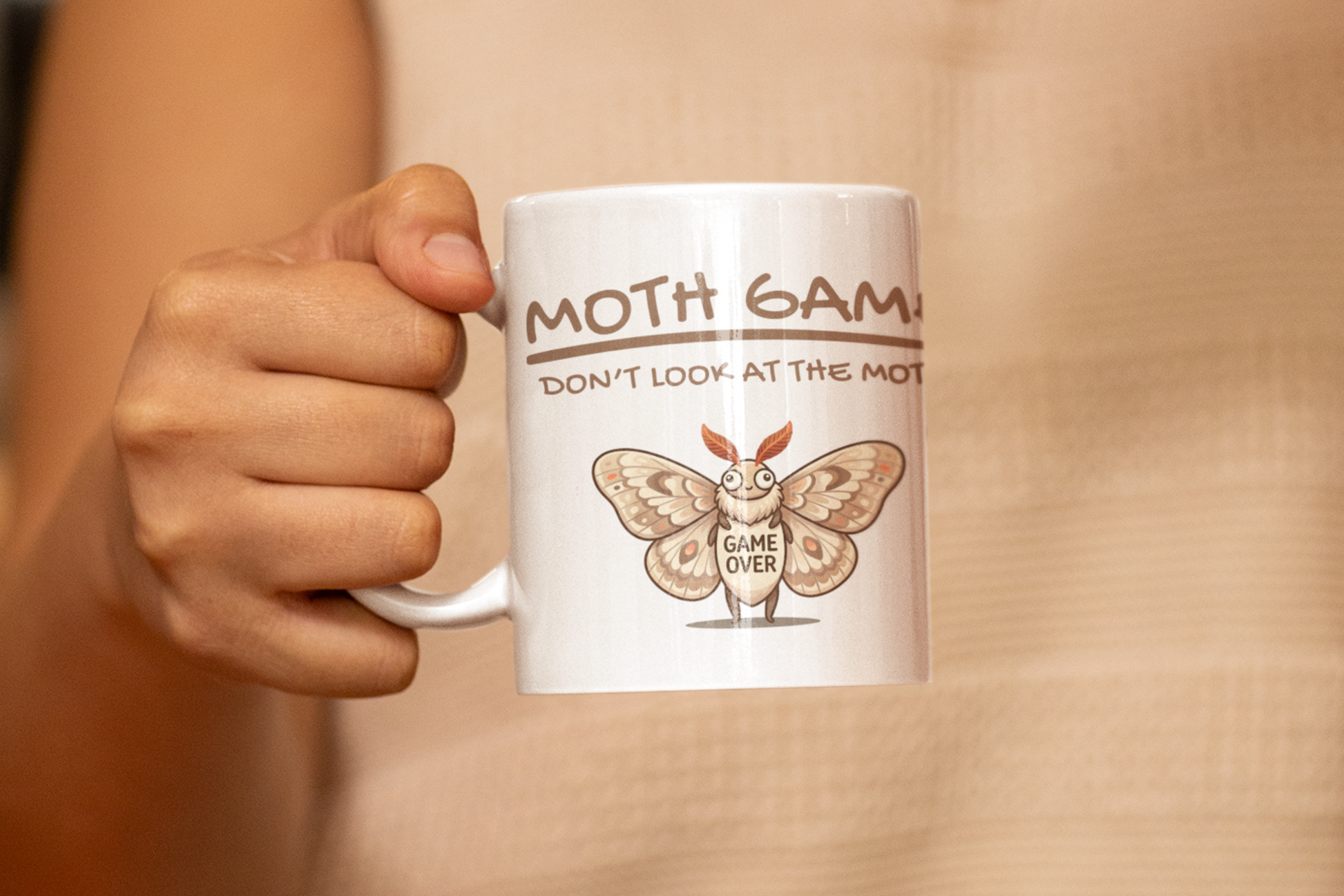 Person holding a white Moth Game Don’t Look At The Moth mug with funny moth meme and Game Over design against a beige background