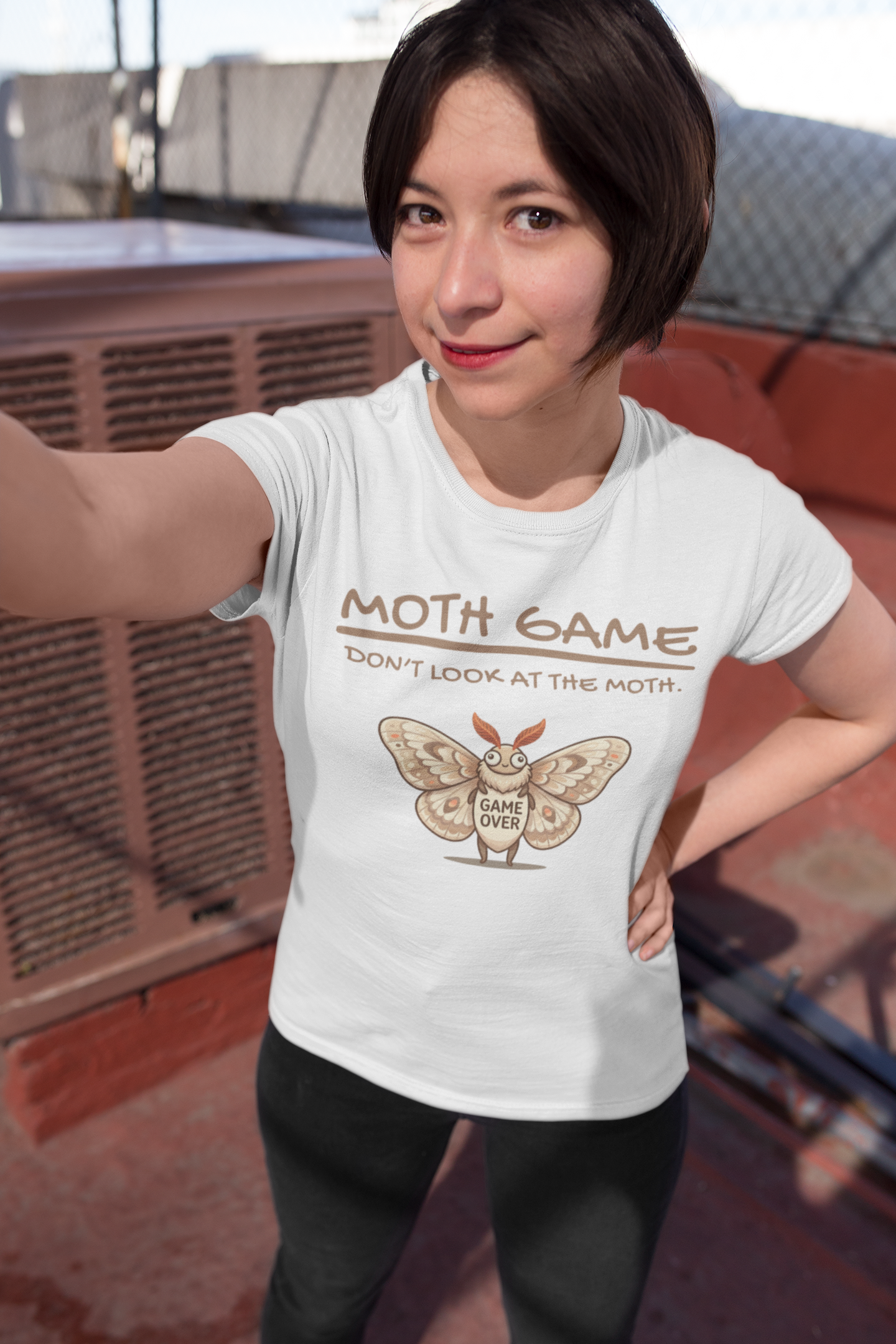 Woman wearing a white Moth Game Don’t Look At The Moth t-shirt with funny moth meme gaming design, standing on a rooftop.