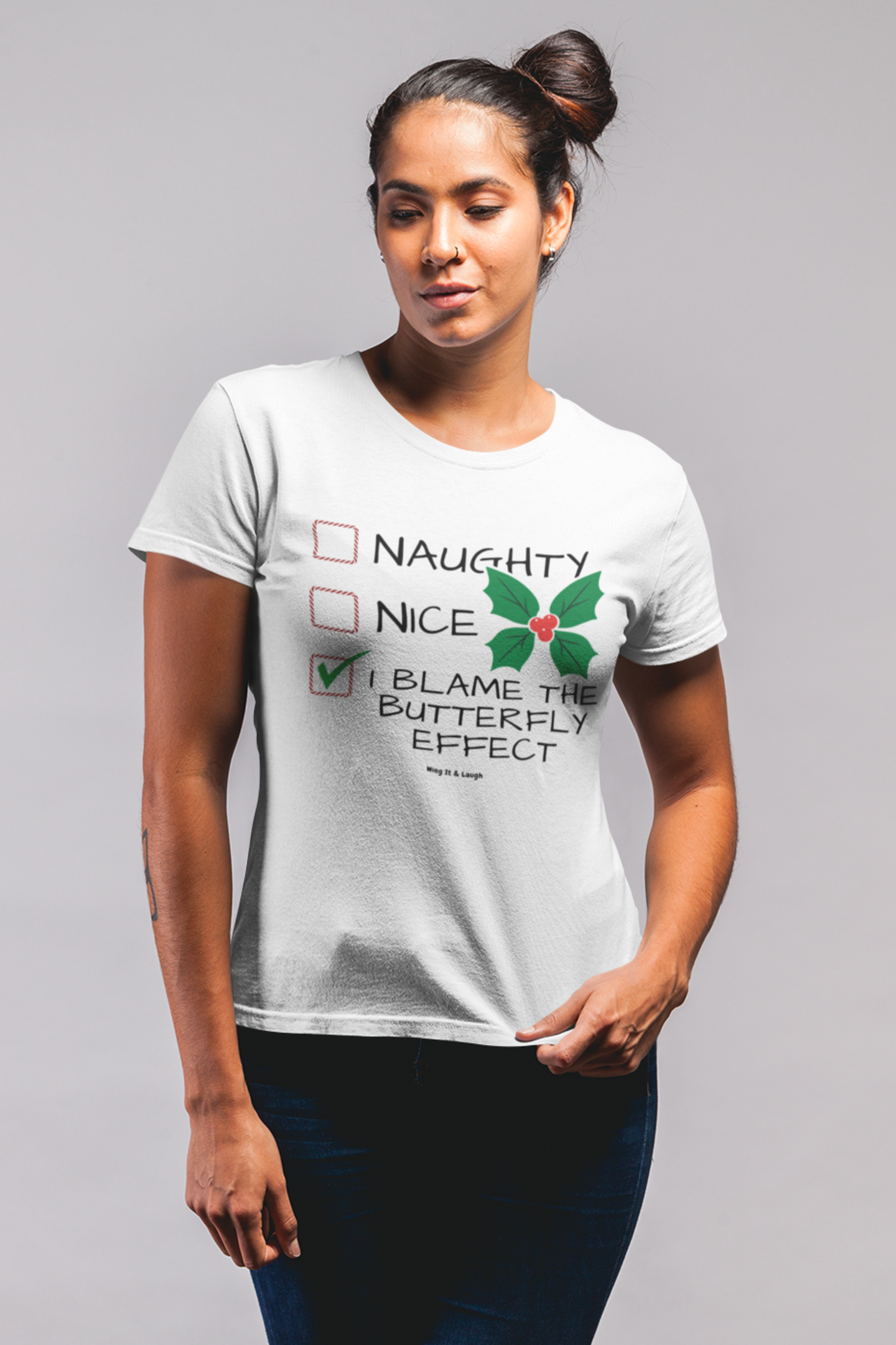 Woman wearing white “I Blame the Butterfly Effect” funny Christmas joke tee on a gray background.