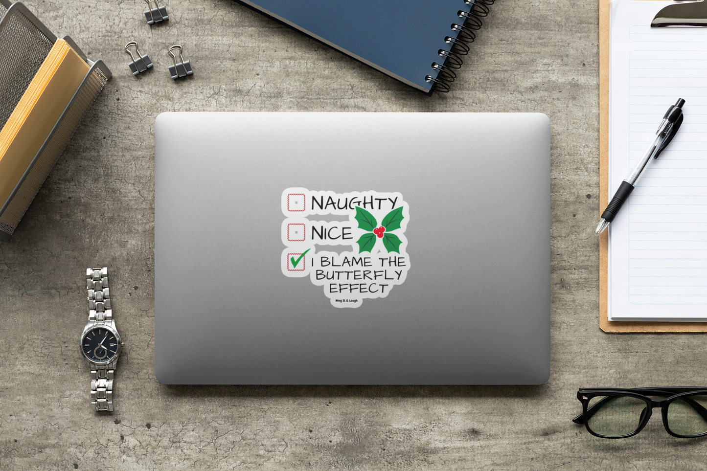 Laptop with a naughty or nice butterfly effect Christmas checklist sticker on a desk with office supplies