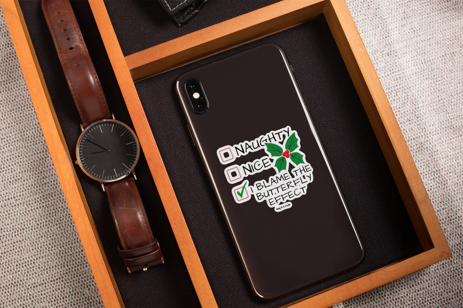 Phone case decorated with naughty or nice butterfly effect Christmas checklist sticker in a wooden box with a watch.