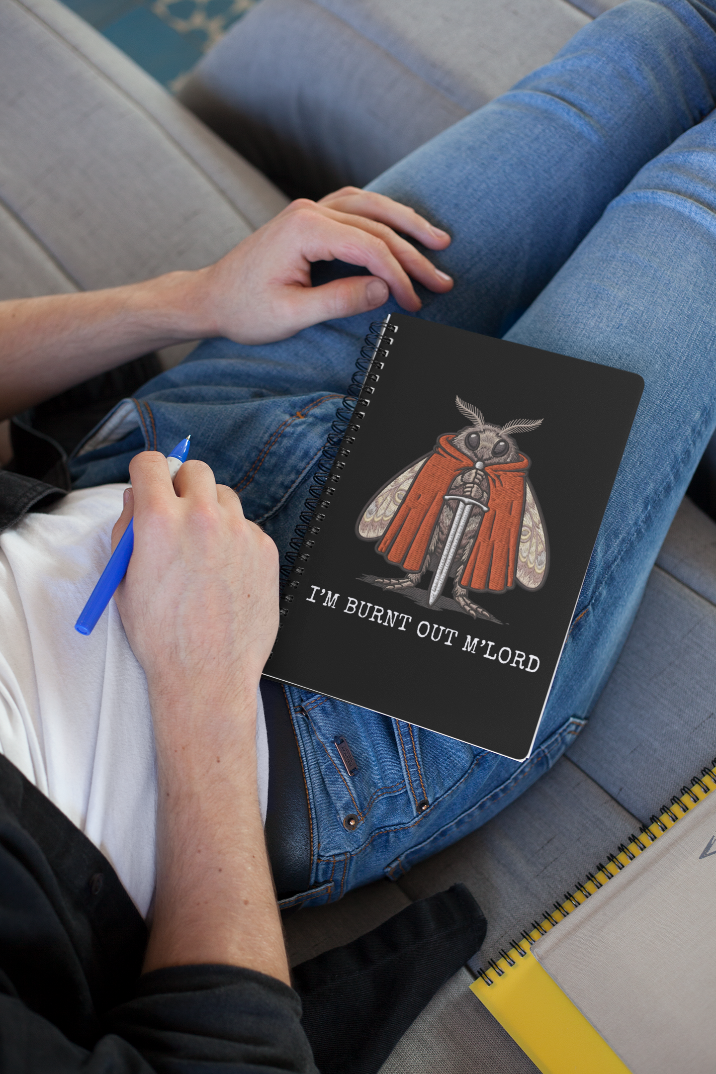 person writing in funny moth notebook with dark humor burnout meme design, sitting on a couch.