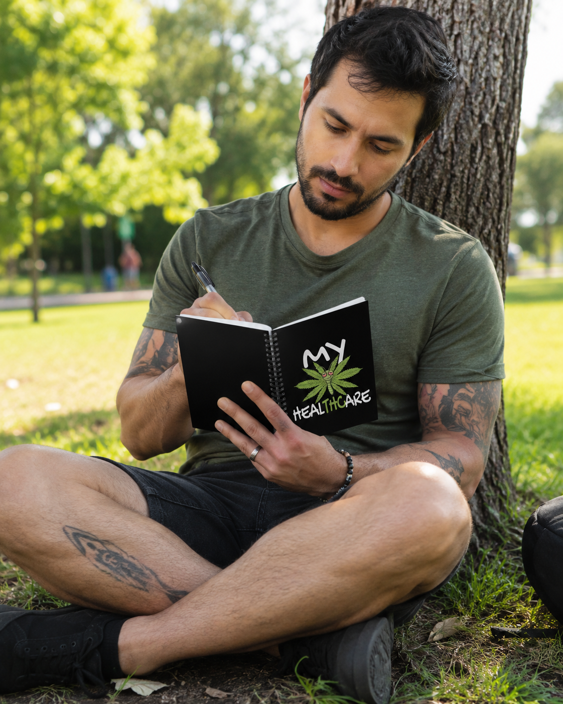 Person writing in a My Healthcare cannabis butterfly spiral notebook outdoors, featuring a funny marijuana leaf cover for weed lovers.