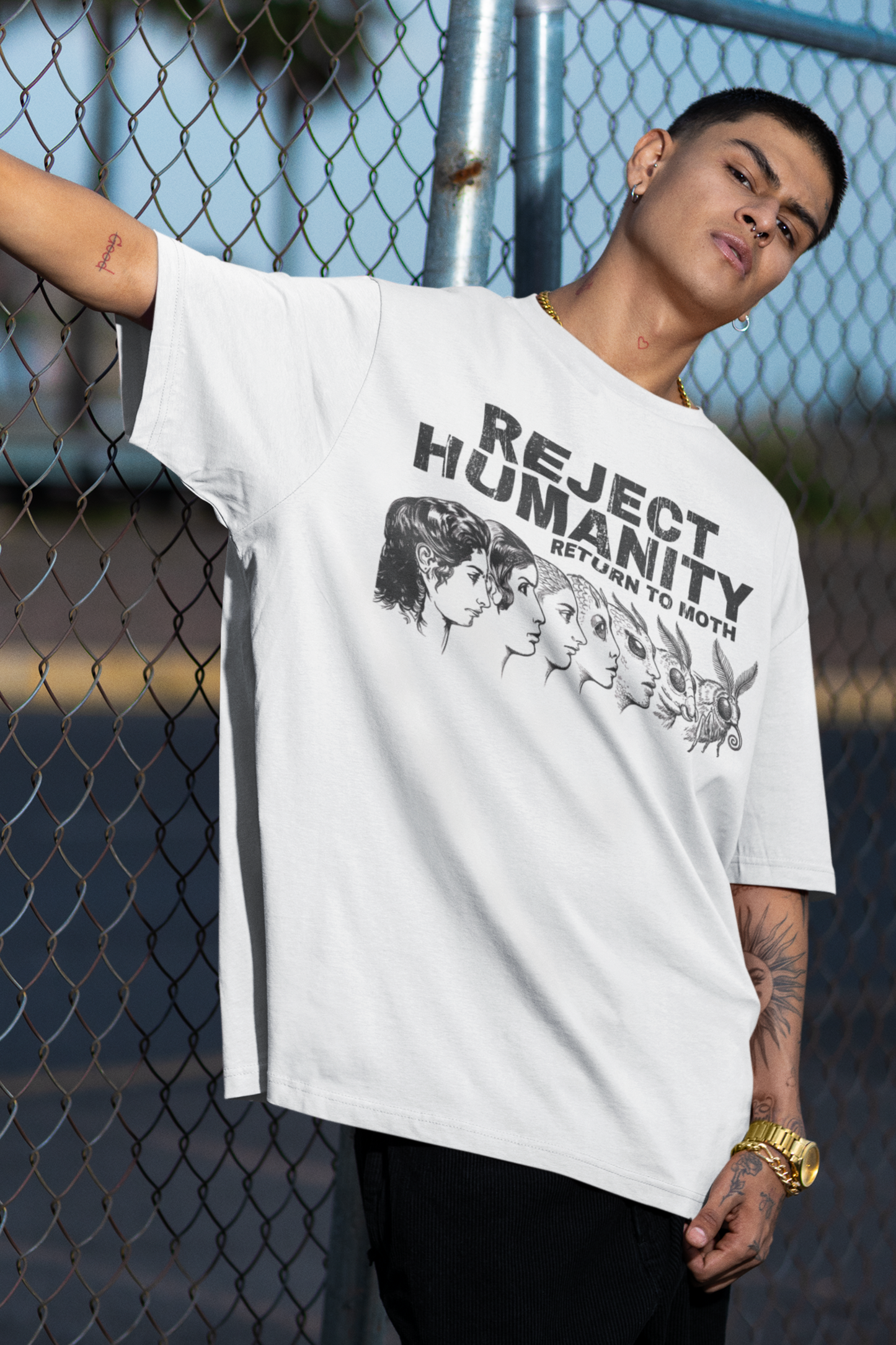 Man wearing weirdcore moth meme shirt with vintage evolution graphic design, standing against a chain-link fence.