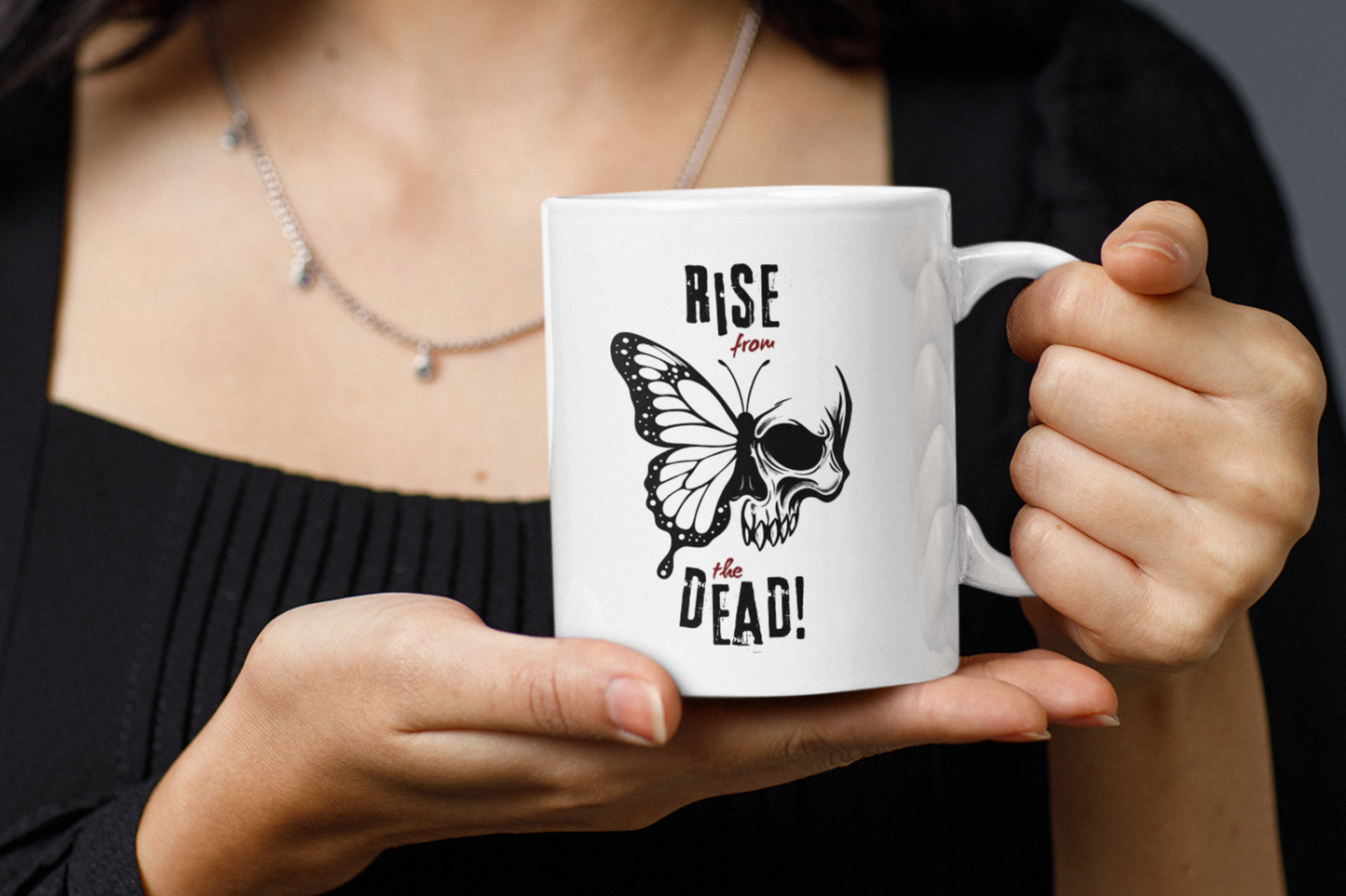 Person holding a white skull-butterfly coffee mug with “Rise from the Dead!” text.