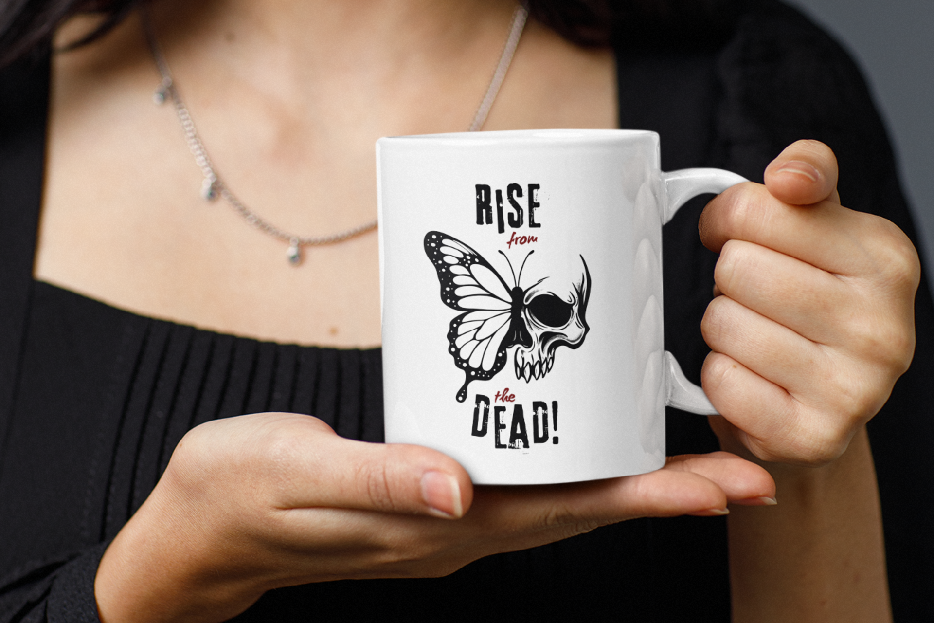 Person holding a white skull-butterfly coffee mug with “Rise from the Dead!” text.