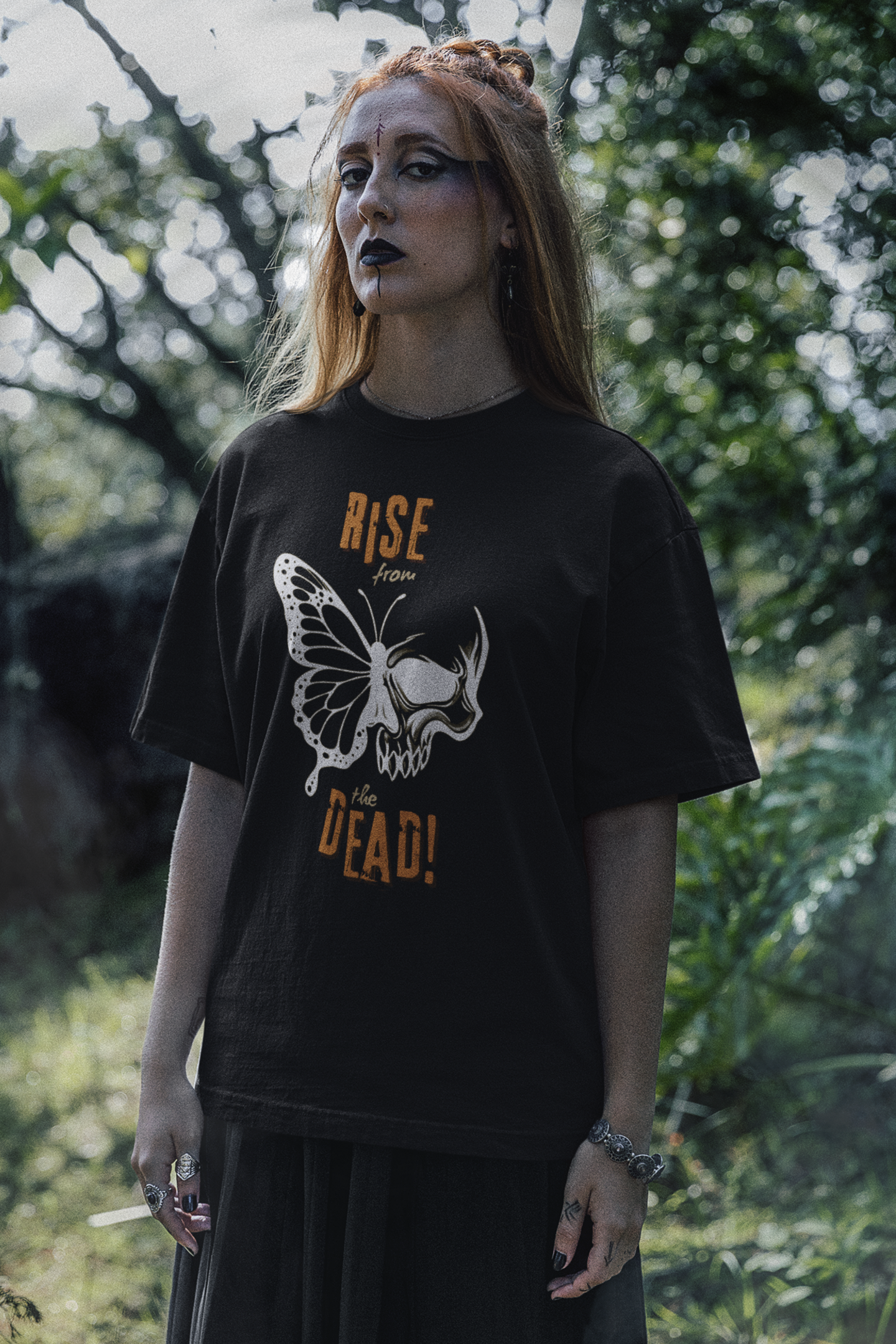 Female model wearing a black skull-butterfly rebirth tee standing outdoors.