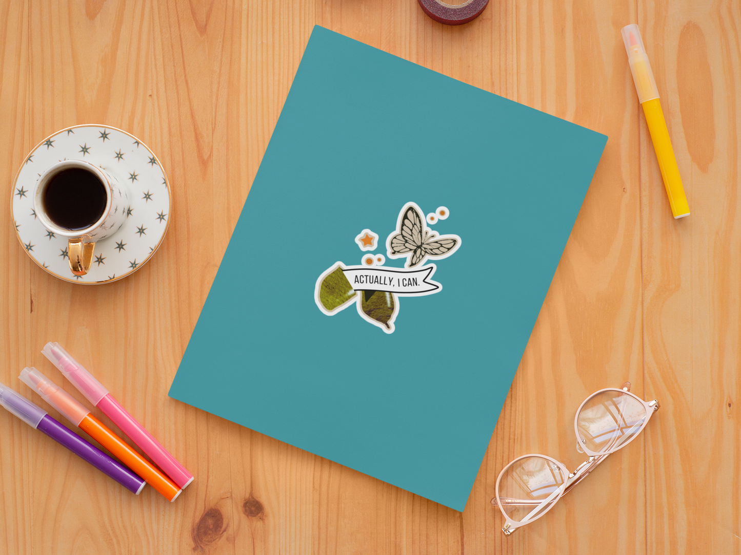 teal notebook with a butterfly design on a wooden surface with stationery items.