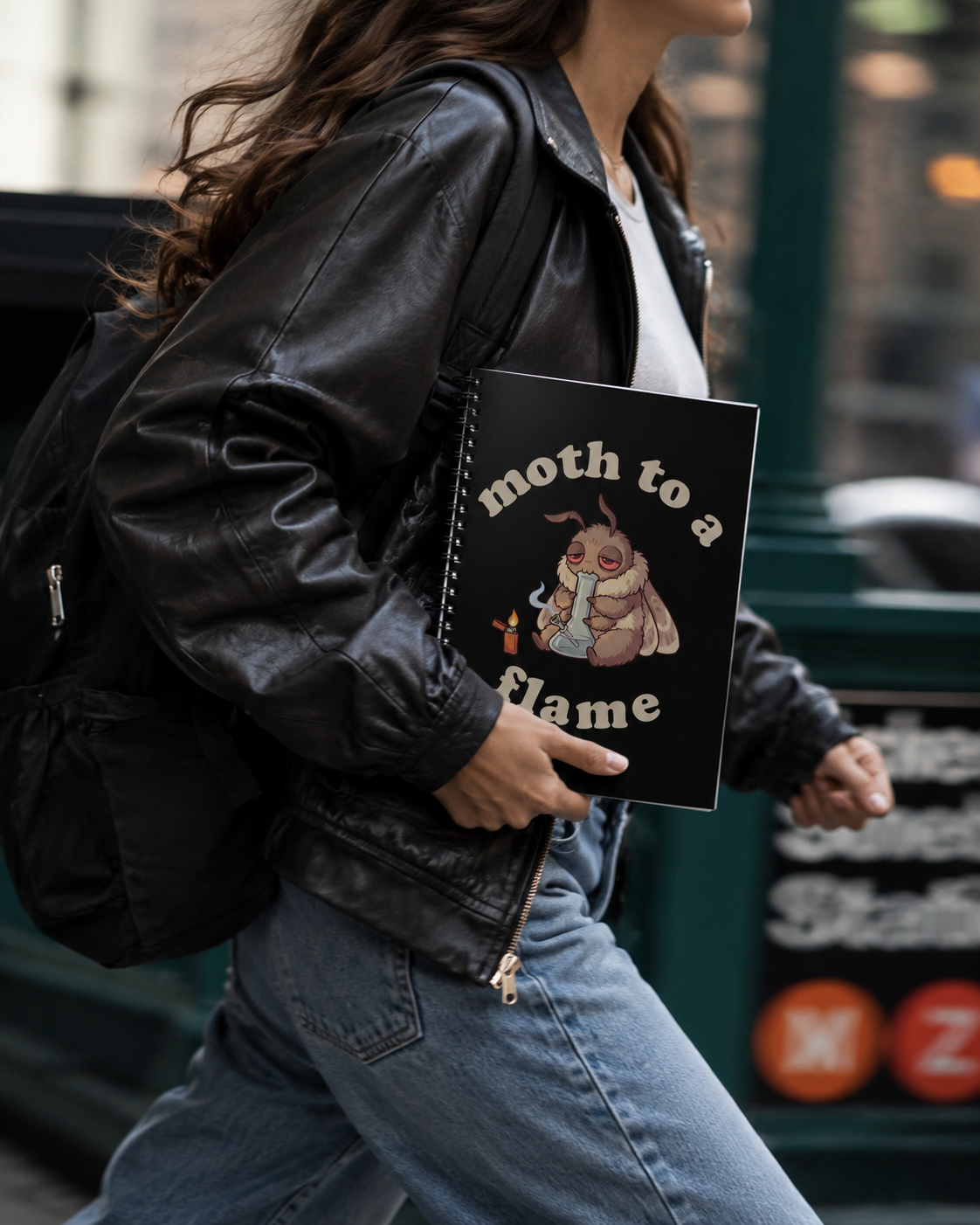 Person carrying a black Moth To a Flame cannabis notebook, featuring a stoner moth graphic for marijuana smokers, moth fans, and 420 journal lovers