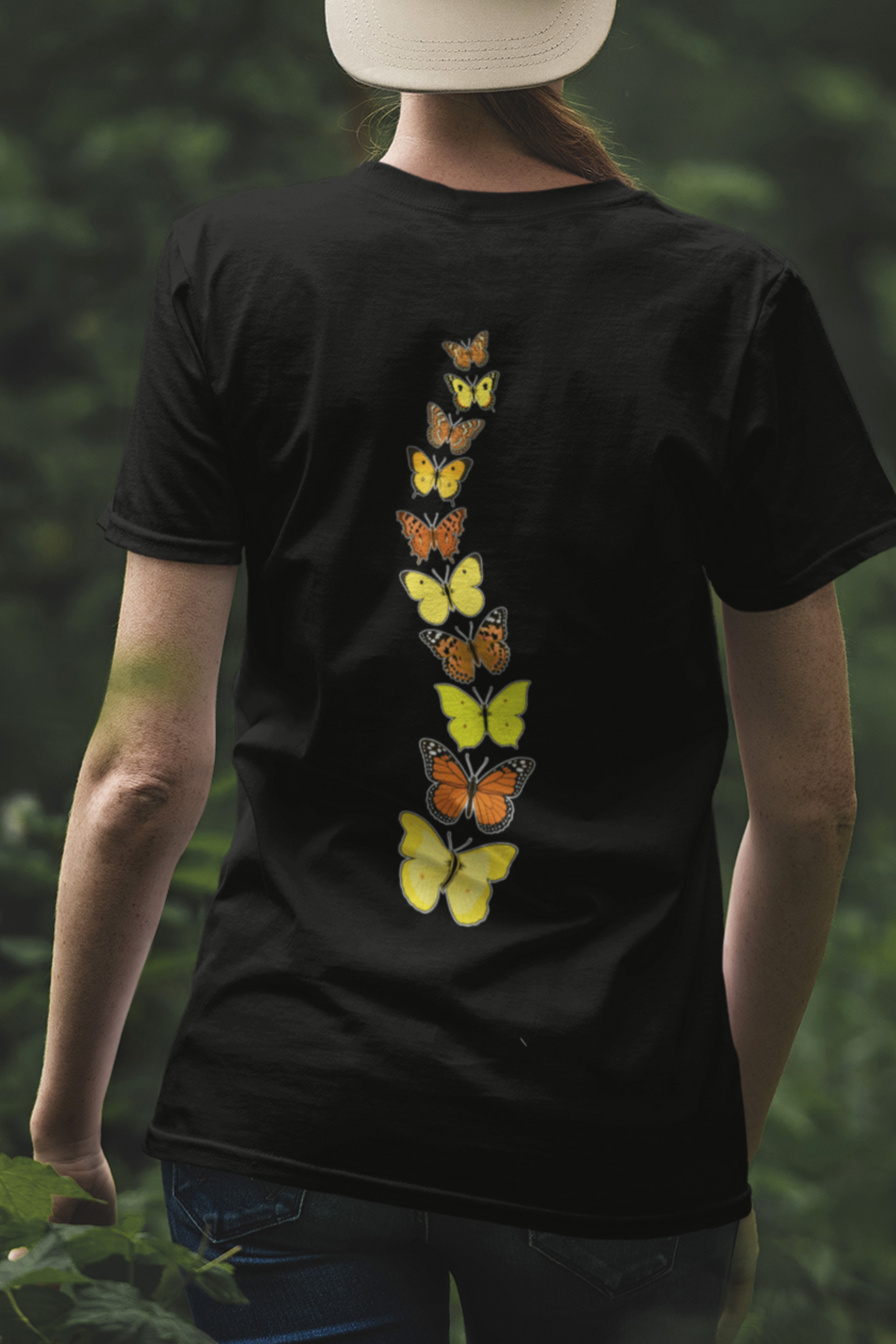 Woman wearing a black butterfly t-shirt outdoors featuring a colorful yellow and orange butterfly back print.