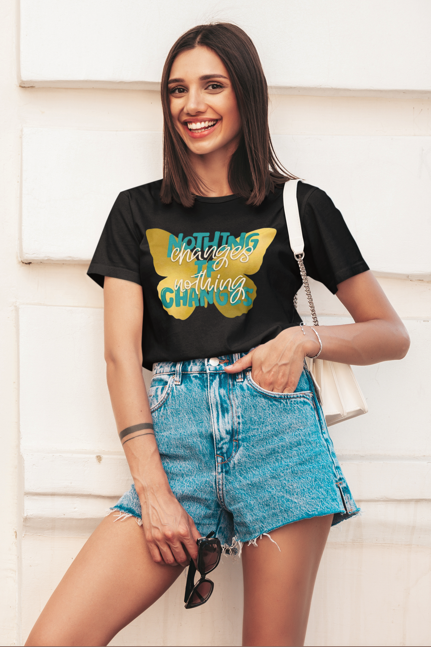 Woman wearing a motivational butterfly t-shirt nothing changes if nothing changes inspirational graphic tee, standing against a light-colored wall.