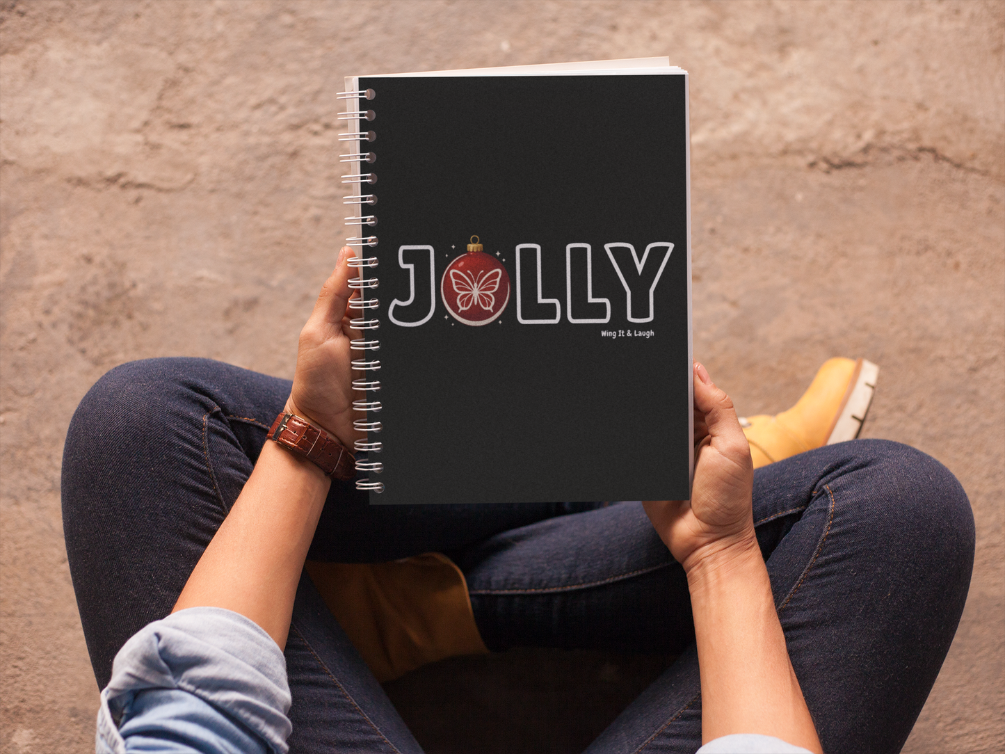 Person holding a black notebook with 'Jolly' holiday branding on a textured surface