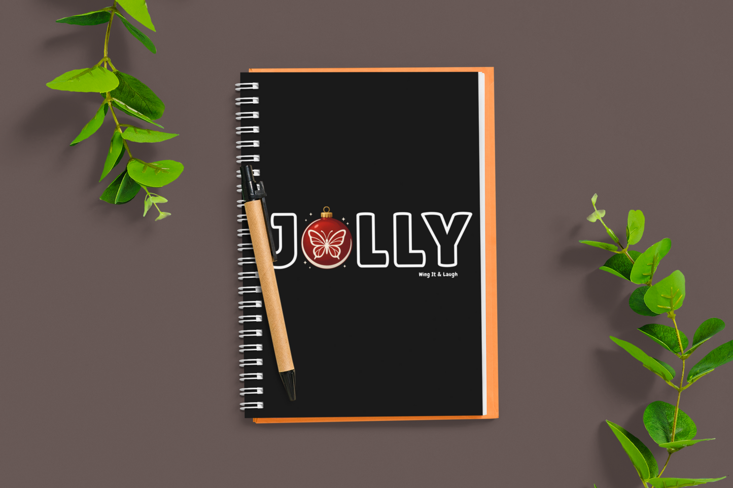 Notebook with 'Jolly' holiday design on a dark background with green leaves