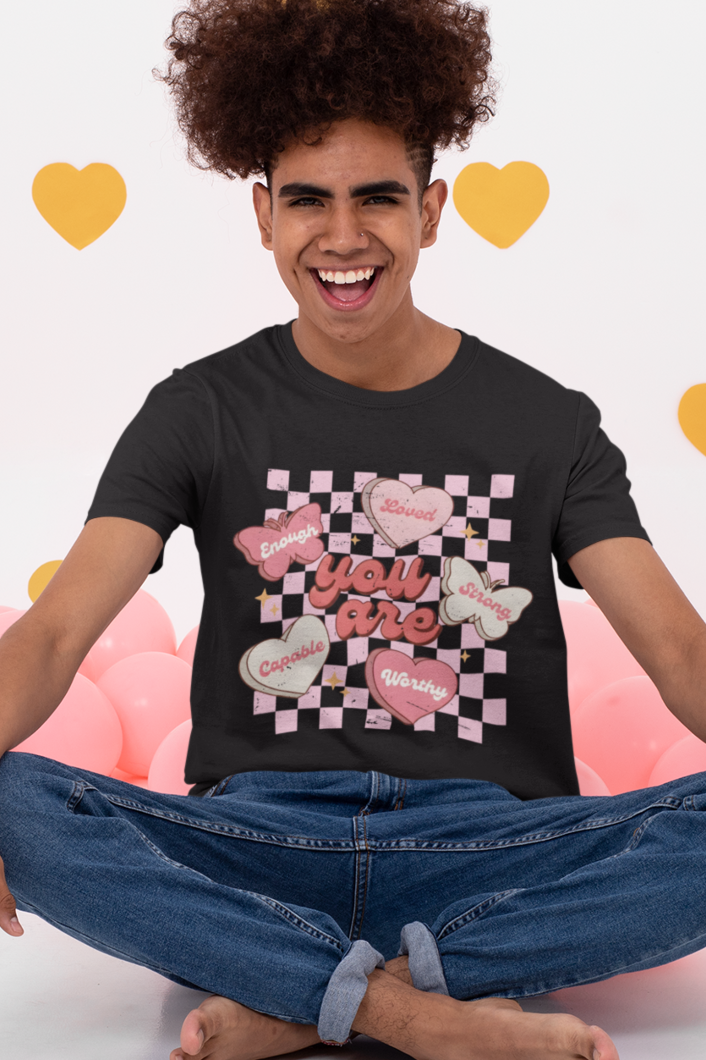 Person wearing a black butterfly affirmation t-shirt with colorful graphics and text, sitting on the floor